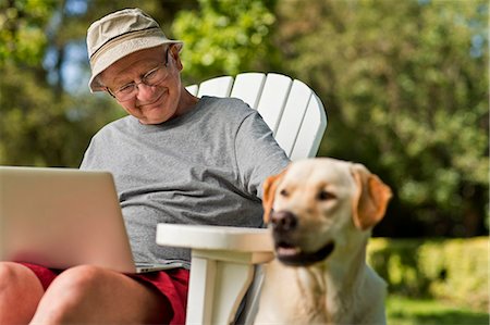 Senior man using his laptop in the garden, with his dog by his side. Stock Photo - Premium Royalty-Free, Code: 6128-08727798