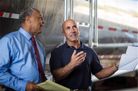 Cheerful mature businessman chats to the yard foreman as they check an oil truck. Stock Photo - Premium Royalty-Free, Code: 6128-08727946