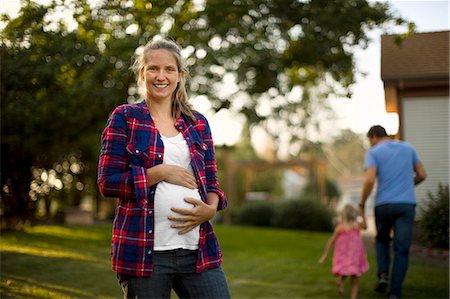 Happy pregnant woman smiling as her family walk in the background. Stock Photo - Premium Royalty-Free, Code: 6128-08727938