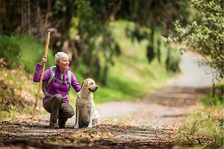senior woman 60 - Portrait of a cheerful mature woman taking a break from hiking in the forest to pet her dog. Stock Photo - Premium Royalty-Free, Code: 6128-08728017