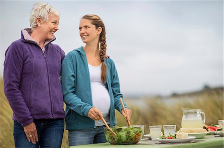 simsearch:6128-08767280,k - Cheerful mature woman chats with her pregnant daughter as they prepare an outdoor lunch. Stock Photo - Premium Royalty-Free, Code: 6128-08728025