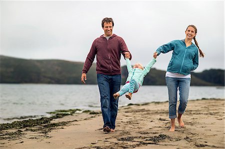 simsearch:6128-08728311,k - Affectionate young couple swing their little girl between them on a walk at the beach. Photographie de stock - Premium Libres de Droits, Code: 6128-08728026