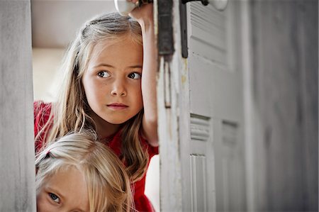 Two young girls peering around a doorframe. Stock Photo - Premium Royalty-Free, Code: 6128-08728298