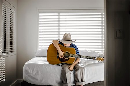 simsearch:6128-08728230,k - Young boy sitting on his bed with his acoustic guitar. Fotografie stock - Premium Royalty-Free, Codice: 6128-08728230