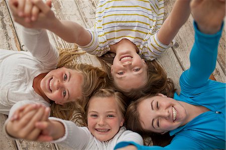 simsearch:649-07648199,k - Portrait of four smiling sisters holding hands while lying close together on a hardwood floor. Stockbilder - Premium RF Lizenzfrei, Bildnummer: 6128-08737669