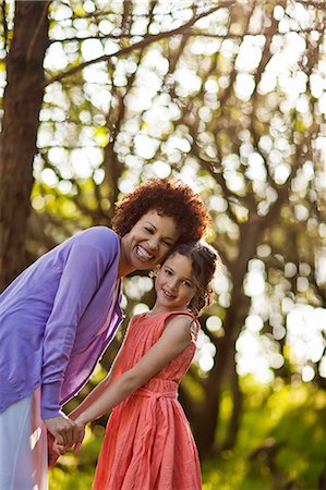 Portrait of a smiling mid adult woman and her daughter holding hands while standing in a forest. Stock Photo - Premium Royalty-Free, Code: 6128-08737629