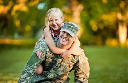 Portrait of a smiling army soldier giving his young daughter a piggy back in their back yard. Photographie de stock - Premium Libres de Droits, Code: 6128-08737835