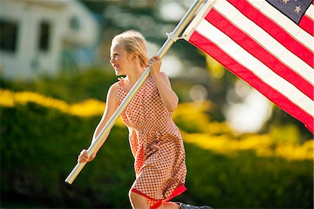 simsearch:6128-08737856,k - Smiling young girl carrying an American flag while running through her back yard. Photographie de stock - Premium Libres de Droits, Code: 6128-08737836