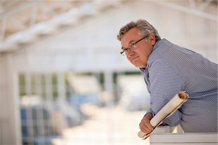 Contemplative mature man leaning on the railing of a balcony while holding rolled up building plans. Stock Photo - Premium Royalty-Free, Code: 6128-08737974
