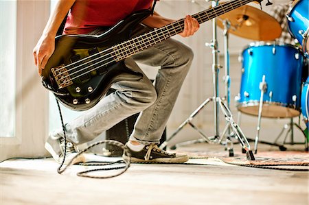 simsearch:6128-08737935,k - Teenage boy crouching while playing a bass guitar next to a drum kit inside a garage. Stock Photo - Premium Royalty-Free, Code: 6128-08737923