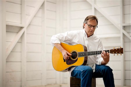 simsearch:6128-08728230,k - Mid adult man playing an acoustic guitar inside a garage. Fotografie stock - Premium Royalty-Free, Codice: 6128-08737929