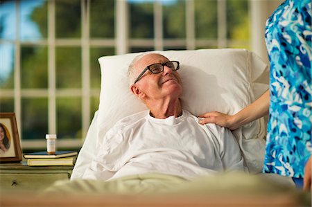 simsearch:6128-08738394,k - Smiling senior man being comforted by a female nurse while lying in bed. Fotografie stock - Premium Royalty-Free, Codice: 6128-08738065