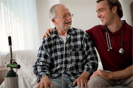 Cheerful elderly man with a nasal tube speaking with a male nurse at his hospital bed. Stock Photo - Premium Royalty-Free, Code: 6128-08738172