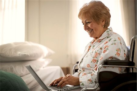 Smiling senior woman having fun using a laptop while sitting in a wheelchair. Stock Photo - Premium Royalty-Free, Code: 6128-08738187