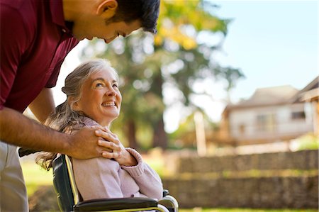 simsearch:6128-08738394,k - Smiling senior woman being comforted by a male nurse while sitting in a wheelchair inside a park. Fotografie stock - Premium Royalty-Free, Codice: 6128-08738197