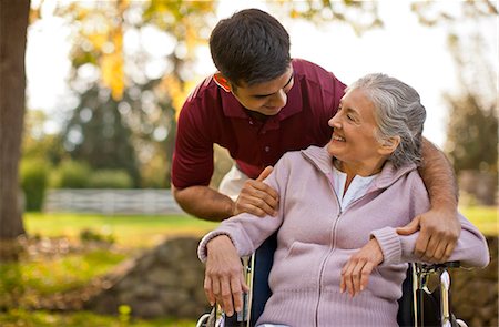 simsearch:6128-08738394,k - Smiling senior woman being comforted by a male nurse while sitting in a wheelchair inside a park. Fotografie stock - Premium Royalty-Free, Codice: 6128-08738196