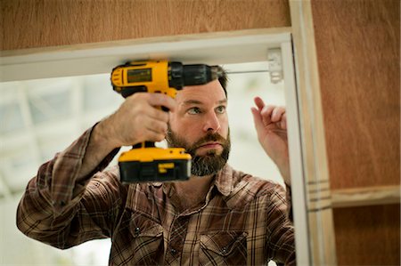 simsearch:6128-08728169,k - Mid adult man concentrating as he holds an electric drill while mending a door frame. Stock Photo - Premium Royalty-Free, Code: 6128-08738259