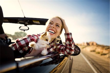 Laughing young woman sitting in the passenger seat of a convertible car with her small dog on a road trip. Stock Photo - Premium Royalty-Free, Code: 6128-08738359