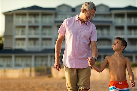simsearch:6128-08728313,k - Father smiling and talking with his young son as they hold hands and walk on the beach at sunset. Stock Photo - Premium Royalty-Free, Code: 6128-08738481