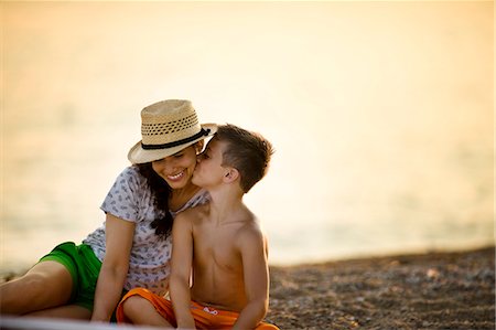 Boy kisses his mother's cheek  on the beach at sunset. Photographie de stock - Premium Libres de Droits, Code: 6128-08738482