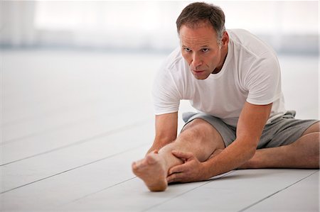 Focused mid adult man stretching leg while practicing yoga. Foto de stock - Sin royalties Premium, Código: 6128-08738427