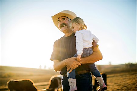 simsearch:6128-08766768,k - Cowboy rancher holding his toddler daughter in his arms while they are out on the ranch. Foto de stock - Sin royalties Premium, Código: 6128-08738557