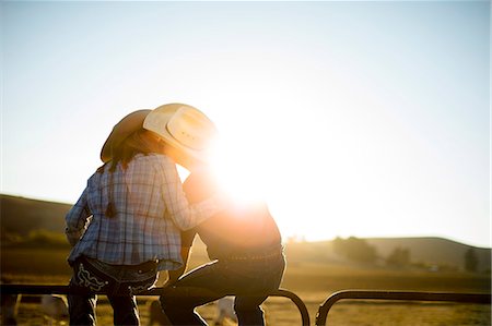 Farmer and his wife sitting on a fence at their ranch and kissing at sunset. Stock Photo - Premium Royalty-Free, Code: 6128-08738555