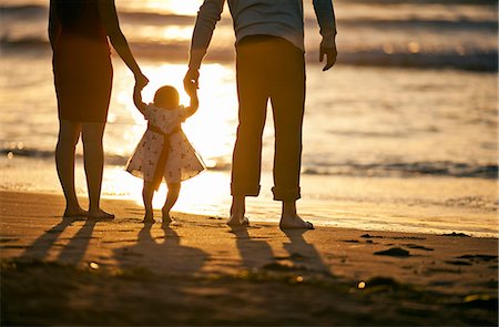 evening dress on beach - Young parents support their baby daughter between them as she takes her first steps on the beach at sunset. Stock Photo - Premium Royalty-Free, Code: 6128-08738572