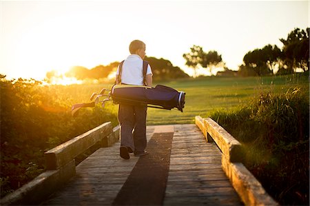 recreation golfing - Young boy carrying a bag of golf clubs. Stock Photo - Premium Royalty-Free, Code: 6128-08738512