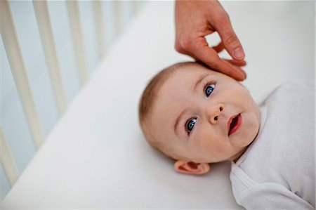 simsearch:6102-08558784,k - Cute baby boy gazing up out of his cot as his young mother places a gentle hand on his cheek. Foto de stock - Sin royalties Premium, Código: 6128-08738653