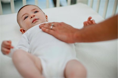 parent crib baby - Cute baby boy gazing up out of his cot as his young mother places a gentle hand on his chest. Stock Photo - Premium Royalty-Free, Code: 6128-08738651