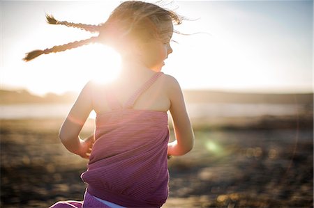 pictures of girls at beach rear - Smiling young girl's pigtails swing as she runs towards the sunlight. Stock Photo - Premium Royalty-Free, Code: 6128-08738657