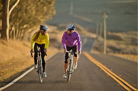 simsearch:6128-08738600,k - Two smiling young women cycling together down a country road. Stock Photo - Premium Royalty-Free, Code: 6128-08738600