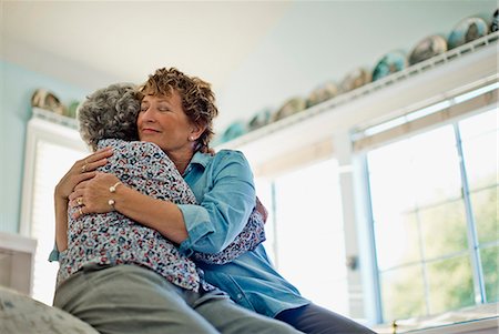 Mature woman gently smiles as she embraces her elderly mother as they sit on the edge of a comfortable bed. Foto de stock - Sin royalties Premium, Código: 6128-08738613