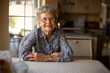 simsearch:6128-08727873,k - Portrait of a cheerful elderly woman sitting alone at her kitchen table. Photographie de stock - Premium Libres de Droits, Code: 6128-08738630
