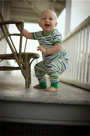 simsearch:6128-08780390,k - Young baby laughing while holding himself up next to a wicker chair. Foto de stock - Royalty Free Premium, Número: 6128-08840933