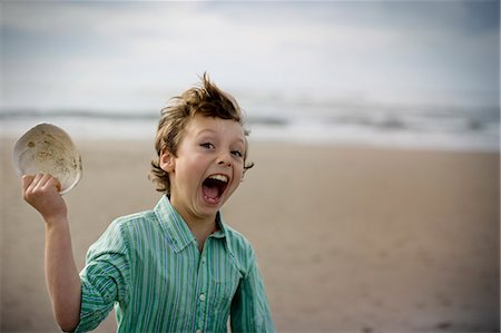 simsearch:6108-06907274,k - Portrait of a young boy with his mouth open while holding up a large shell at the beach. Foto de stock - Sin royalties Premium, Código: 6128-08840935