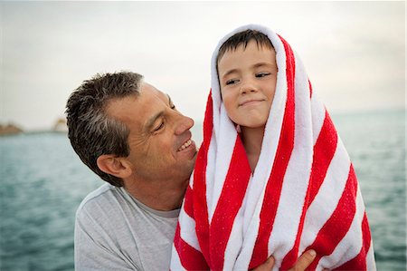 simsearch:6128-08825403,k - Smiling man looking at his son who is wrapped in a striped towel. Stock Photo - Premium Royalty-Free, Code: 6128-08841050