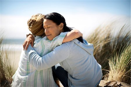 simsearch:6128-08748166,k - Two women hugging while sitting at the beach. Photographie de stock - Premium Libres de Droits, Code: 6128-08841006