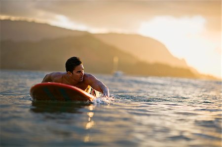 surfer male adult middle aged - Male surfer lies on his board,  looks over his shoulder and paddles in anticipation of a coming wave. Stock Photo - Premium Royalty-Free, Code: 6128-08825367