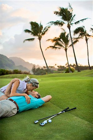 simsearch:695-03379005,k - Smiling female golfer sitting on the green leans over to kiss a smiling male golfer lying on the ground next to her with his arm around her. Photographie de stock - Premium Libres de Droits, Code: 6128-08825369