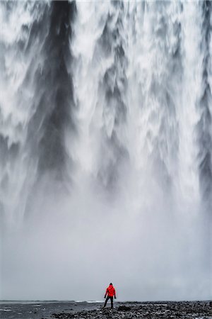 skogafoss waterfall - Skogafoss waterfall, Skoga, Iceland. A man in red jacket is standing under the Skogafoss waterfall Foto de stock - Sin royalties Premium, Código: 6129-09044021