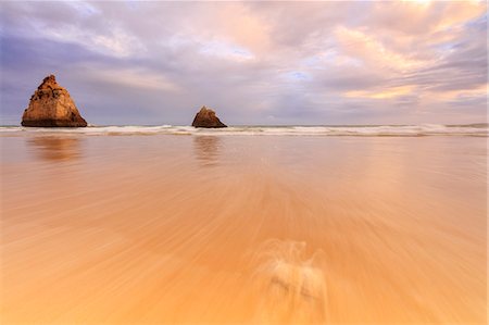 Pink sky at sunset on cliffs and sandy beach surrounded by the clear sea Praia Dos Tres Irmaos Portimao Algarve Portugal Europe Foto de stock - Sin royalties Premium, Código: 6129-09044890