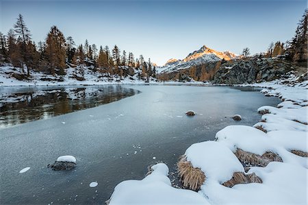 Sasso Moro peak at dawn reflects itself on the iced waters of Mufulé Lake. Valmalenco, Valtellina, Sondrio, Lombardy, Italy, Europe. Foto de stock - Royalty Free Premium, Número: 6129-09057716