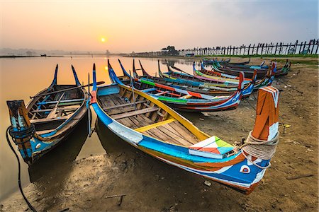 Amarapura, Mandalay region, Myanmar. Colorful boats moored on the banks of the Taungthaman lake at sunrise, with the U Bein bridge in the background. Foto de stock - Royalty Free Premium, Número: 6129-09057890