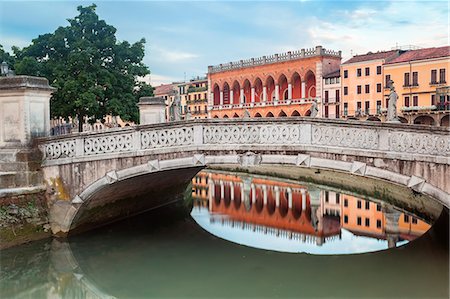 simsearch:879-09034212,k - Prato della Valle, the Loggia Amulea, Padua. Prato della Valle, one of the symbols of Padua is a great elliptical square characterized by a green island in the center, called Memmia Island, surrounded by a canal. Foto de stock - Sin royalties Premium, Código: 6129-09057925