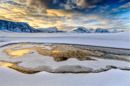 The golden sunrise reflected in a pool of the clear sea where the snow is almost melted. Haukland Lofoten Islands Norway Europe Stock Photo - Premium Royalty-Free, Code: 6129-09058140