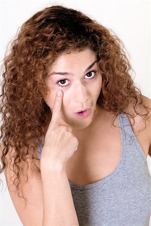 Portrait of a young woman pointing at her eye Stock Photo - Premium Royalty-Free, Code: 625-00838092