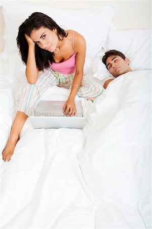 sleeping bed full body - High angle view of a young woman using a laptop with a young man sleeping beside her Stock Photo - Premium Royalty-Free, Code: 625-00841828