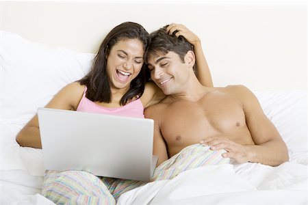 Young couple sitting on a bed looking at a laptop Stock Photo - Premium Royalty-Free, Code: 625-00841822